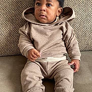 Noé participe au concours pour gagner de l'argent avec cette photo : toddler, child, sitting, hoodie, pants, sneakers, white_shoes, couch, indoor, curly_hair, casual_clothing, young_child, portrait, comfortable, looking_away, cozy, home, furniture, expression, relaxed