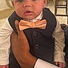 Ali is registered to the contest to win money with this photo: baby, child, tuxedo, bow_tie, hand, indoor, formal_wear, person, face, portrait, curly_hair, earrings, table, chair, dining_room, adult_hand, curious_expression, suit, white_shirt, event