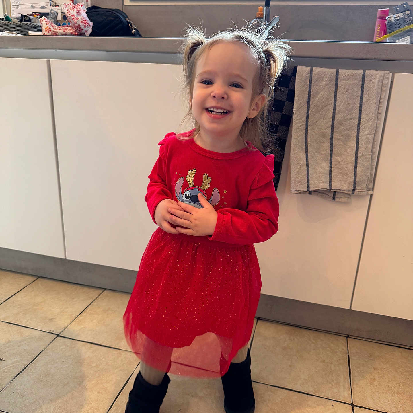 Layannah participe au concours pour gagner de l'argent avec cette photo : toddler, child, smiling, red_dress, pigtails, indoors, kitchen, tile_floor, boots, cabinet, sink, towel, window, happy, person, young_child, long_sleeves, cute, standing, home