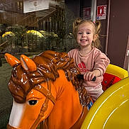 Layannah participe au concours pour gagner de l'argent avec cette photo : child, toddler, smiling, pigtails, carousel_horse, orange_horse, toy, ride, yellow, pink_clothing, indoor, window, nighttime, happy, person, play, amusement, fun, grip, hair_ties