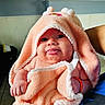 Ariani is registered to the contest to win money with this photo: baby, child, towel, hooded_towel, peach_color, skin, hand, tongue, expression, smile, person, indoor, fabric, cuddle, cute, cozy, wrapping, human, infant, playful