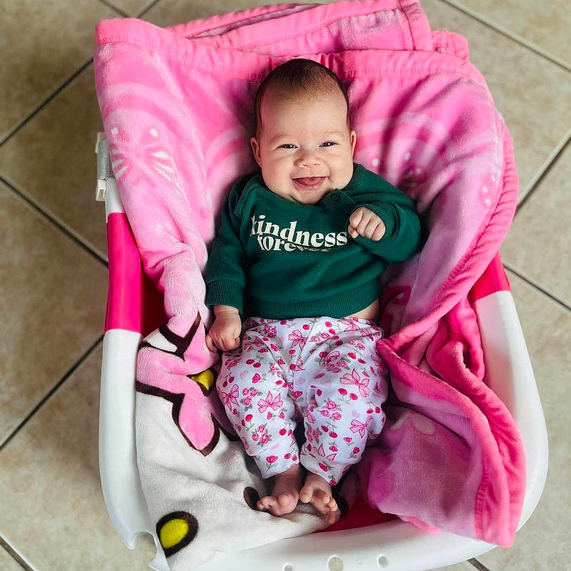 Ariani joined the competition — help win amazing prizes! baby, smiling, child, blanket, basket, floor, tile, clothing, green_sweater, pink_blanket, happy, cute, infant, person, indoors, portrait, feet, head, sitting, cozy