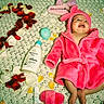 baby, pink_robe, flower_petals, number_two, blanket, baby_care_products, bottle, baby_bottle, baby_girl, happy_baby, lying_down, indoors, celebration, soft_texture, toddler, smiling, headwear, baby_accessory, cute, infant