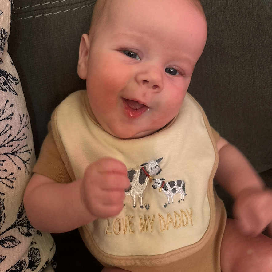 Easton is registered to the contest to win money with this photo: adorable, arm, baby, bib, closeup, clothing, couch, eyes, fabric, face, hand, happy, indoor, infant, onesie, pacifier, portrait, seated, smiling, soft_skin