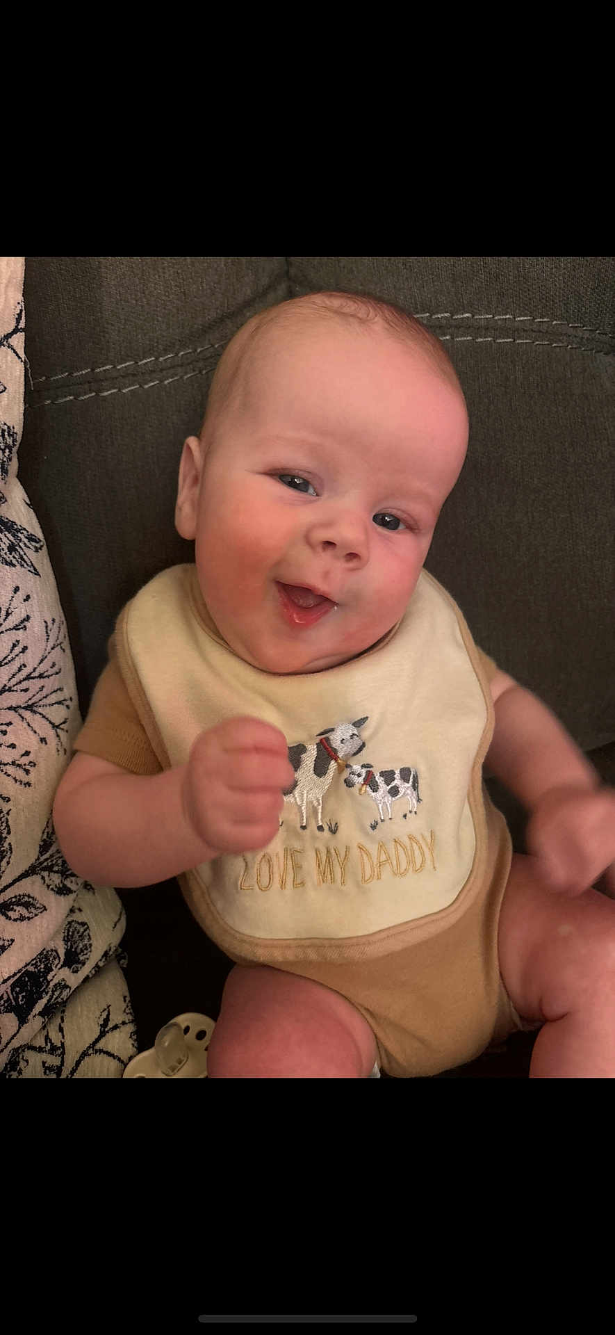 Easton is registered to the contest to win money with this photo: baby, infant, smiling, bib, couch, fabric, pacifier, hand, arm, eyes, face, portrait, indoor, adorable, soft_skin, clothing, onesie, seated, happy, closeup