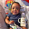 baby, smile, milk_bottle, curly_hair, blue_onesie, baby_chair, colorful, toy, infant, happy, indoors, cute, child, seat, face, milk, holding, portrait, young_child, playful