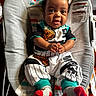 baby, child, infant, smiling, clapping, socks, curly_hair, baby_seat, patterned_clothing, indoor, wooden_floor, colorful_background, happy, cute, portrait, person, playful, seat, hands, eyes