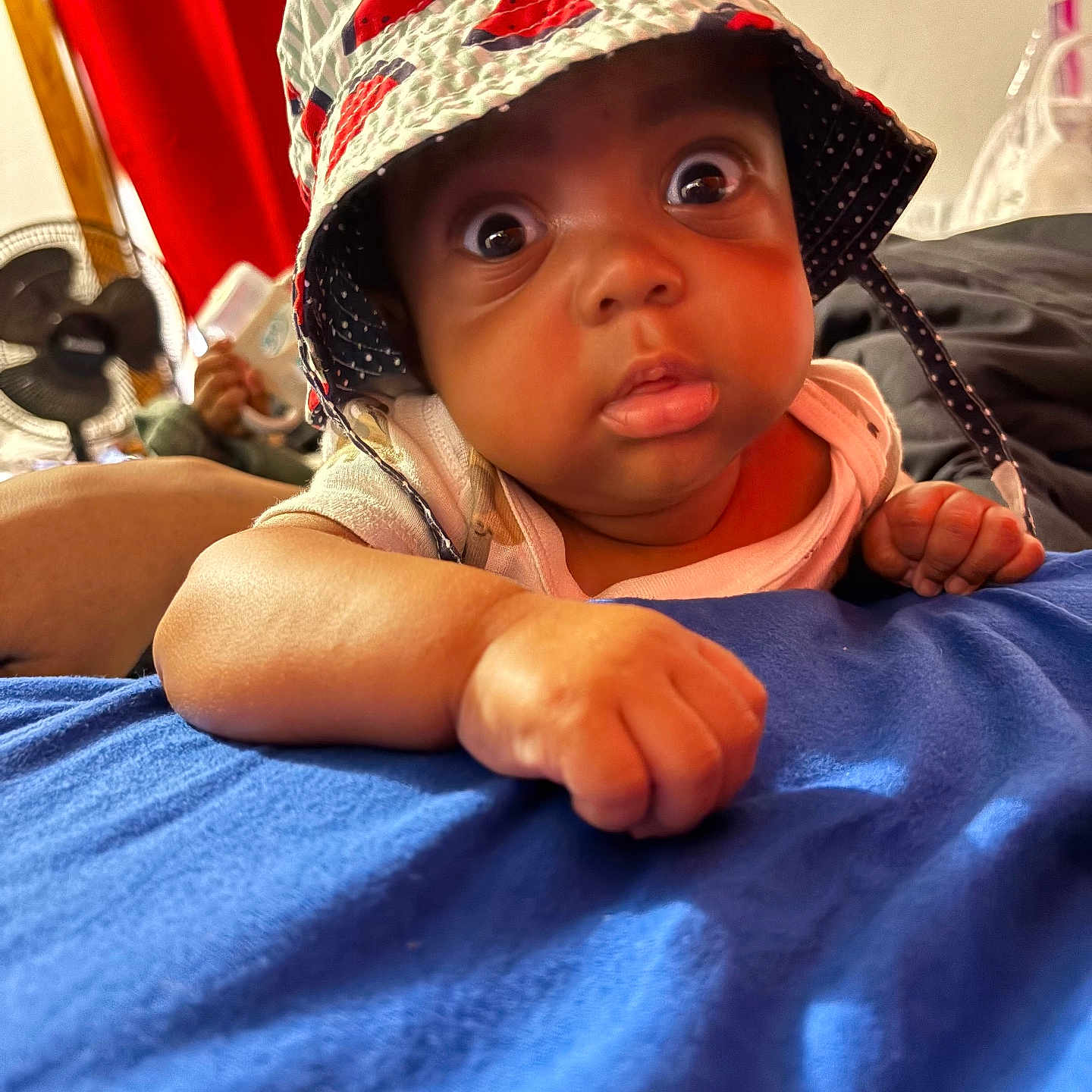 Saviaire joined the competition — help win amazing prizes! baby, child, infant, hat, bucket_hat, wide_eyes, blue_blanket, indoor, curious, surprised, face, hand, red_curtain, fan, bed, clothing, portrait, expression, cute, skin