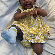 Nayvee is registered to the contest to win money with this photo: baby, child, smiling, yellow_dress, headband, white_blanket, sock, happy, infant, cute, lying_down, playful, floral_pattern, toddler, one_person, indoors, skin, face, hands, feet
