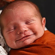 Blaise is registered to the contest to win money with this photo: baby, blanket, bokeh, close_up, cozy, cuddly, fabric, face, indoors, infant, newborn, orange, peaceful, photography, portrait, sleeping, sleepy, smiling, soft_lighting, swaddled