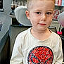 child, boy, haircut, shirt, spiderman, sequin, salon, chair, bottle, product, shelf, haircare, indoor, casual_clothing, short_hair, portrait, sitting, cute, kid, young