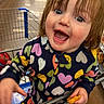 toddler, child, shopping_cart, grocery_store, snack, happy, smiling, colorful_clothing, hearts_pattern, indoor, person, cute, young_child, holding_food, retail, aisle, casual, playful, fun, bright