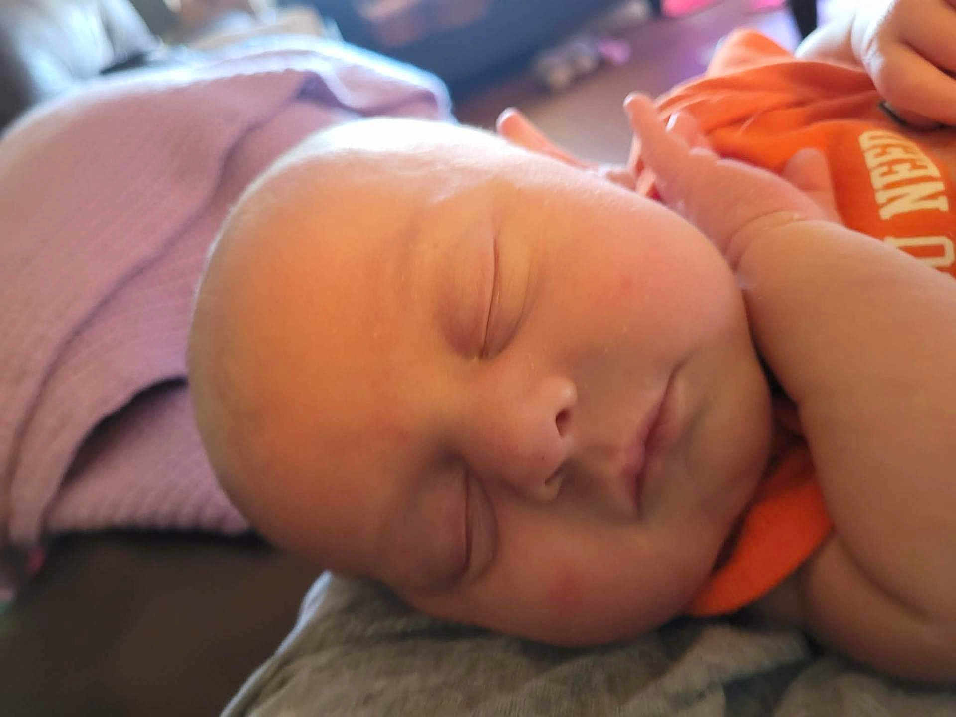 Richard is registered to the contest to win money with this photo: baby, sleeping, face, hand, closeup, infant, blanket, orange_clothing, peaceful, skin, portrait, newborn, child, soft, resting, indoors, cute, person, head, relaxing