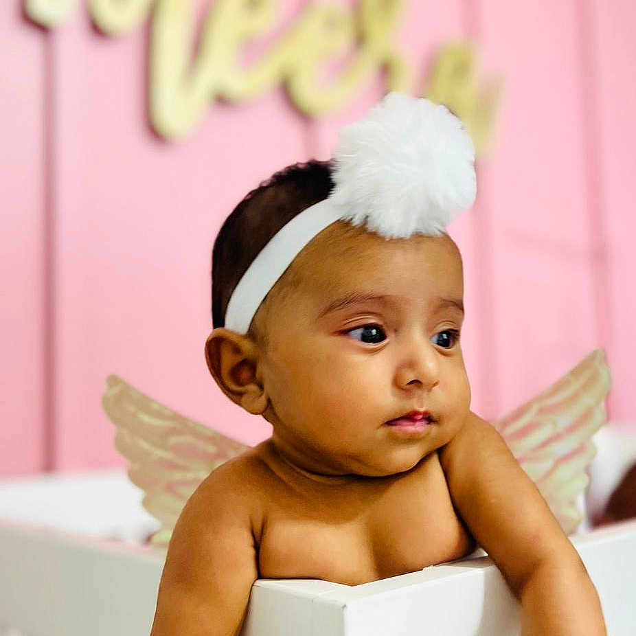 Meera is registered to the contest to win money with this photo: accessories, baby, bathing, bodypart, clothing, crib, face, finger, furniture, hand, happy, head, headband, indoors, infantbed, newborn, person, photography, portrait, smile
