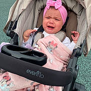 Avia is registered to the contest to win money with this photo: baby, child, crying, stroller, blanket, headband, pink, toy, outdoor, seat, fabric, person, expression, upset, clothing, infant, playground, comfort, sitting, accessory