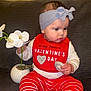 baby, child, headband, bib, valentines_day, flower, orchid, plant, pot, couch, striped_pants, red, white, sitting, indoors, clothing, person, cute, holding, portrait
