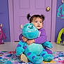 blue_monster, cartoon_monsters, child, colorful_blanket, cute, decorations, door, floor, happy, hugging, indoor, monster_theme, pigtails, playroom, plush_toy, purple_pajamas, smiling, soft_toy, toddler, young_child
