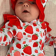 Daisy-Mae is registered to the contest to win money with this photo: baby, infant, strawberry_pattern, hat, bonnet, clothing, onesie, red, white, cute, lying_down, blanket, portrait, child, face, expression, fabric, soft, closeup, indoors