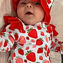 baby, infant, strawberry_pattern, hat, bonnet, clothing, onesie, red, white, cute, lying_down, blanket, portrait, child, face, expression, fabric, soft, closeup, indoors