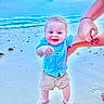 toddler, child, beach, ocean, sand, smiling, holding_hand, blue_shirt, shorts, barefoot, water, sky, waves, person, happy, outdoor, summer, playing, family, vacation
