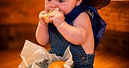 Weston is registered to the contest to win money with this photo: baby, child, food, bread, sandwich, hat, denim, overalls, blue_bandana, sitting, indoor, wood_floor, basket, cute, eating, portrait, infant, chubby_cheeks, appetizer, clothing