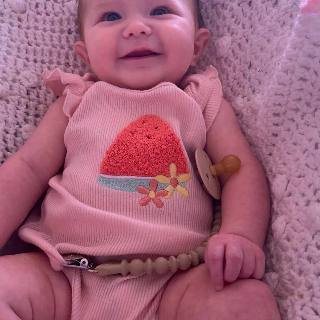 Isabella is registered to the contest to win money with this photo: baby, child, comfortable, cozy, cute, face, hand, happy, indoor, infant, knit_blanket, legs, pacifier, pink_clothing, portrait, sitting, skin, smiling, soft_texture, young