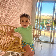 Amelio participe au concours pour gagner de l'argent avec cette photo : child, boy, indoor, rattan_chair, shorts, patterned_clothing, spiky_hair, window, sliding_door, outdoor_view, pool_area, sunlight, floor, wallpaper, geometric_pattern, furniture, seated, casual, expression, curious
