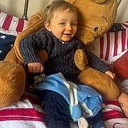 Maryus a rejoint le concours — aidez-le/la à gagner de superbes lots ! toddler, child, teddy_bear, blanket, bed, bedding, striped_socks, smile, happy, cozy, indoor, plush, clothing, sweater, pants, toy, cute, person, face, portrait