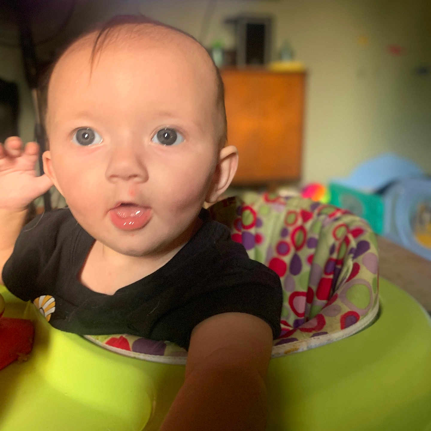 Annabeth is registered to the contest to win money with this photo: baby, baby_walker, black_shirt, blurred_background, child, clothing, colorful, curious, expression, eyes, face, furniture, hand, indoor, infant, mouth, person, portrait, room, young