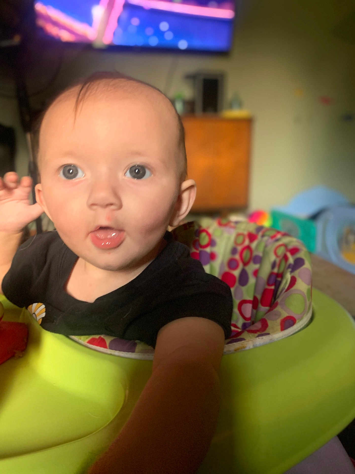 Annabeth is registered to the contest to win money with this photo: baby, infant, face, eyes, mouth, hand, baby_walker, colorful, indoor, child, person, curious, expression, clothing, black_shirt, furniture, blurred_background, room, young, portrait