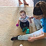 baby, child, toddler, woman, carpet, floor, ball, toy, sitting, playing, indoor, person, clothing, sock, trash_bin, hairband, jeans, barefoot, home, interaction