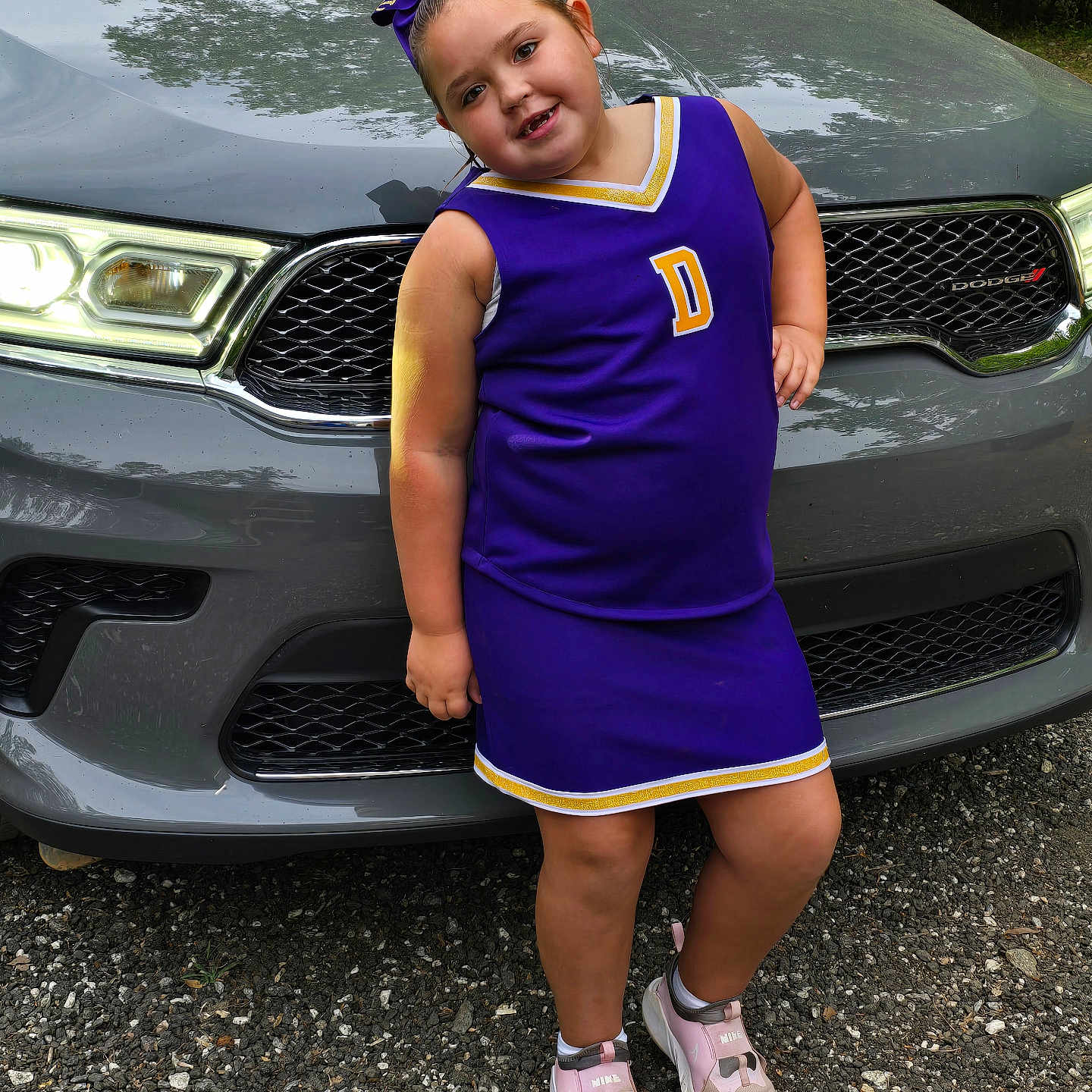 Delilah is registered to the contest to win money with this photo: alloywheel, car, carwheel, child, clothing, dress, face, footwear, head, machine, person, photography, portrait, sandal, shoe, spoke, tire, transportation, vehicle, wheel