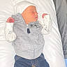 baby, blue_pants, child, clothing, cute, gray_hoodie, hospital_bassinet, indoors, infant, laying_down, newborn, newborn_clothes, peaceful, pillow, portrait, resting, sleeping, small_hands, soft_lighting, white_hat