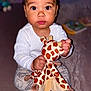 toddler, child, plush_toy, giraffe, baby, pajamas, blanket, indoor, person, cute, face, sitting, looking_at_camera, soft_lighting, toy, small_hand, foot, expression, cozy, young_child