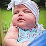 baby, child, headband, bow, outdoor, greenery, pastel_clothing, cute, chubby_cheeks, portrait, soft_skin, infant, holding, person, summer, daylight, closeup, face, expression, young_child