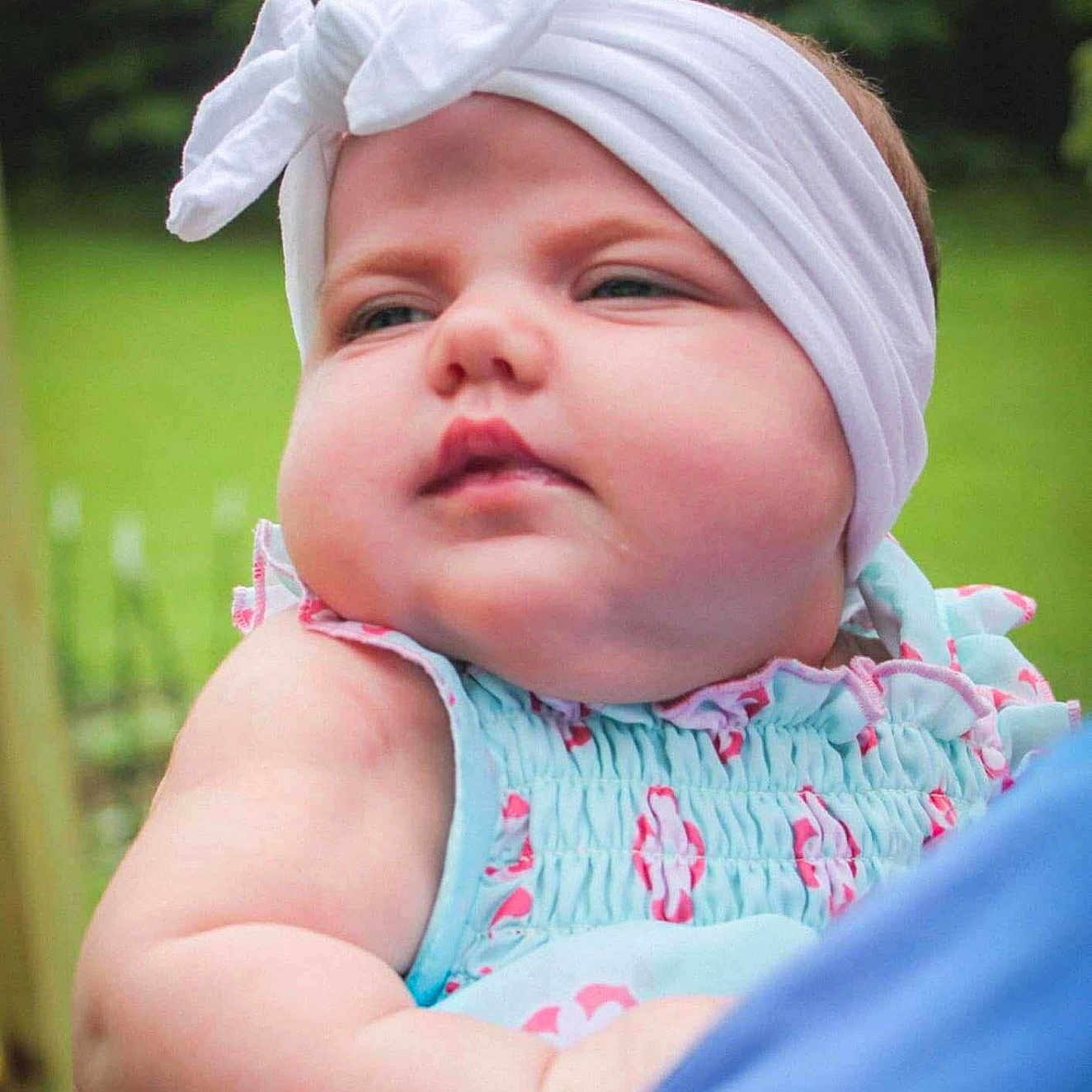 Maddalynn joined the competition — help win amazing prizes! baby, bow, child, chubby_cheeks, closeup, cute, daylight, expression, face, greenery, headband, holding, infant, outdoor, pastel_clothing, person, portrait, soft_skin, summer, young_child