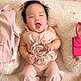 baby, infant, pink_outfit, rose, cushion, plush_toy, handbag, flowers, smiling, happy, lying_down, indoors, cute, child, soft_texture, decor, small_bag, toy, person, portrait