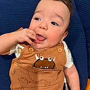 Asher joined the competition — help win amazing prizes! baby, blue_cushion, brown_overall, cheeks, child, clothing, cute, expression, face, finger_in_mouth, hand, happy, indoors, infant, monster_print, portrait, short_hair, sitting, smiling, young_child