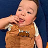 baby, blue_cushion, brown_overall, cheeks, child, clothing, cute, expression, face, finger_in_mouth, hand, happy, indoors, infant, monster_print, portrait, short_hair, sitting, smiling, young_child