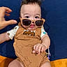 Asher is registered to the contest to win money with this photo: accessory, baby, blue_cushion, child, clothing, cute, expression, fashion, hand, indoor, infant, monster_prints, orange_surface, person, playful, portrait, romper, seated, smile, sunglasses