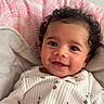 Melody is registered to the contest to win money with this photo: baby, smiling, infant, curly_hair, cozy, blanket, cushion, patterned, pink, white_outfit, floral, portrait, face, child, happy, indoors, cute, closeup, soft, comfortable