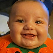 Corey is registered to the contest to win money with this photo: baby, smiling, close_up, face, child, orange_clothing, pumpkin_outfit, happy, cute, infant, drool, indoors, portrait, chubby_cheeks, eyes, head, person, holiday, festive, costume