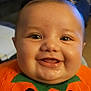 baby, smiling, close_up, face, child, orange_clothing, pumpkin_outfit, happy, cute, infant, drool, indoors, portrait, chubby_cheeks, eyes, head, person, holiday, festive, costume