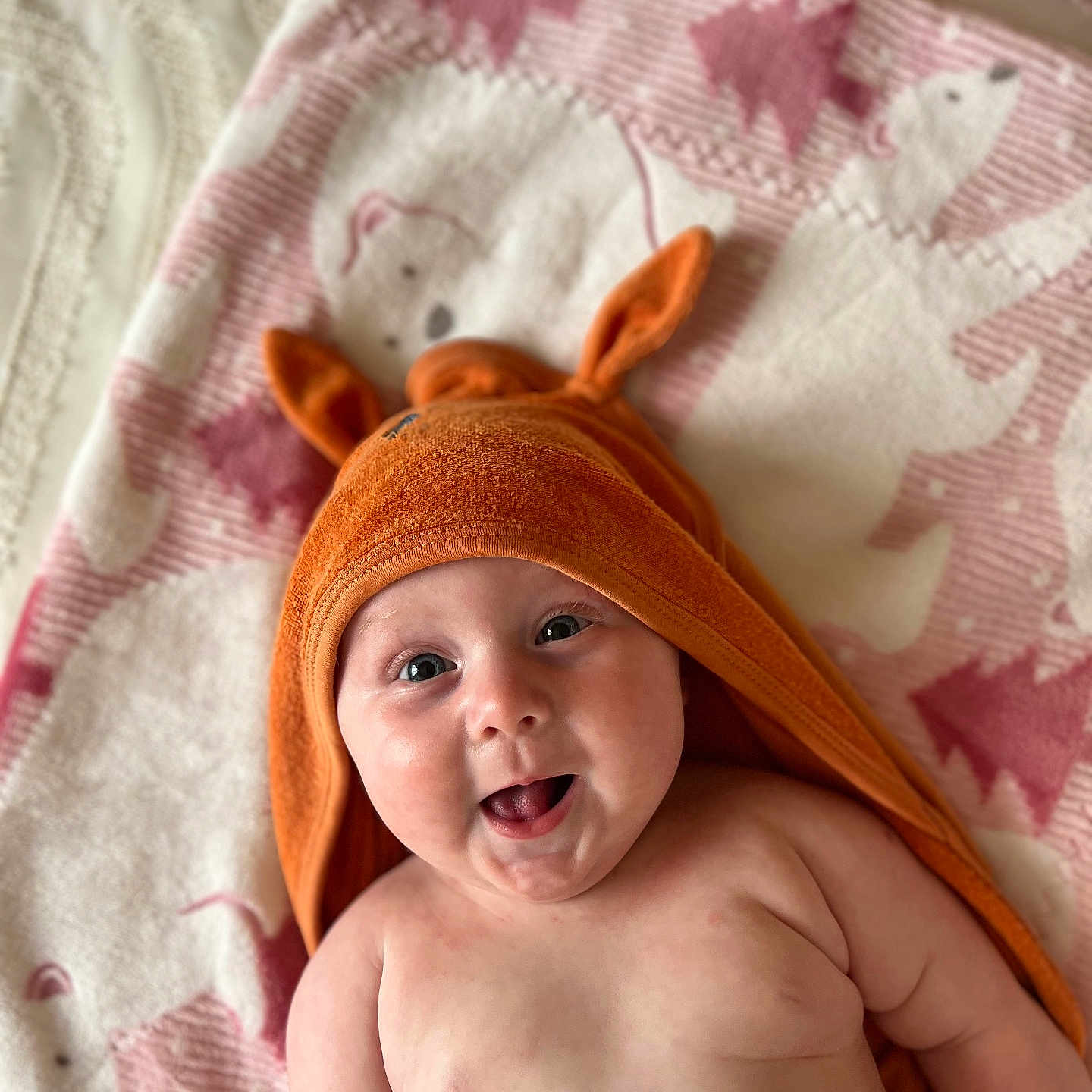 Eva joined the competition — help win amazing prizes! baby, blanket, child, chubby_cheeks, cute, eyes, face, happy, hooded_towel, indoors, infant, lying_down, mouth, orange_towel, pink, playful, polar_bear_pattern, skin, smiling, soft_texture