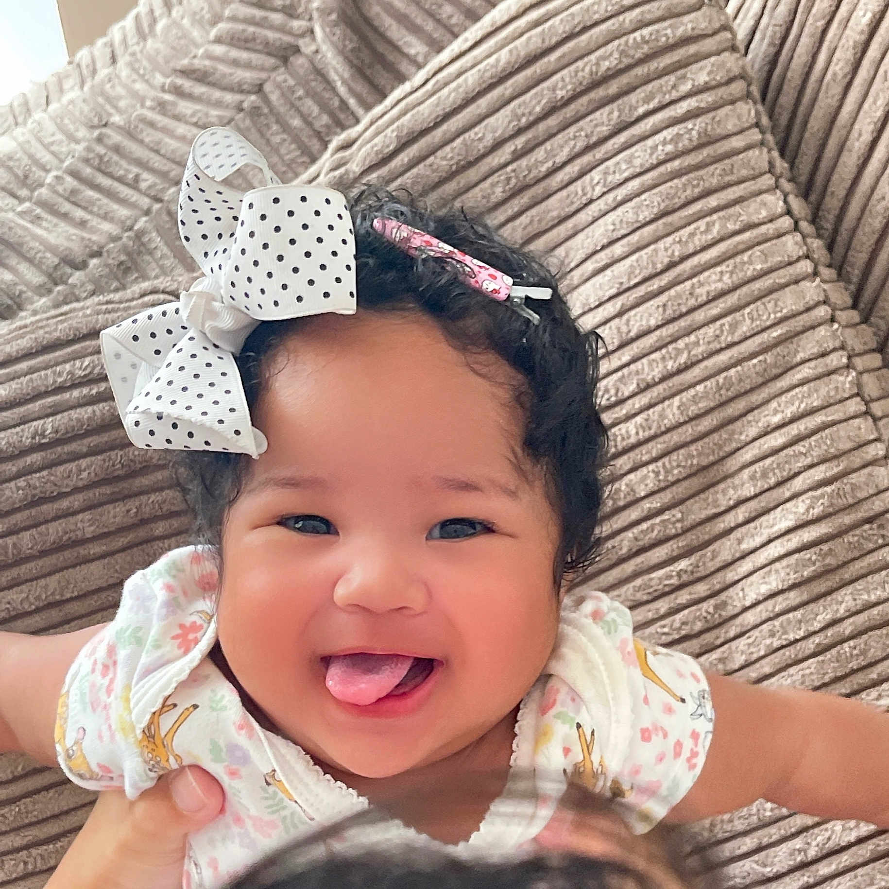 Magdalene is registered to the contest to win money with this photo: baby, bow, child, clothing, couch, curly_hair, cute, face, hair_accessory, hand, happy, indoor, infant, person, playful, portrait, skin, smiling, tongue_out, young