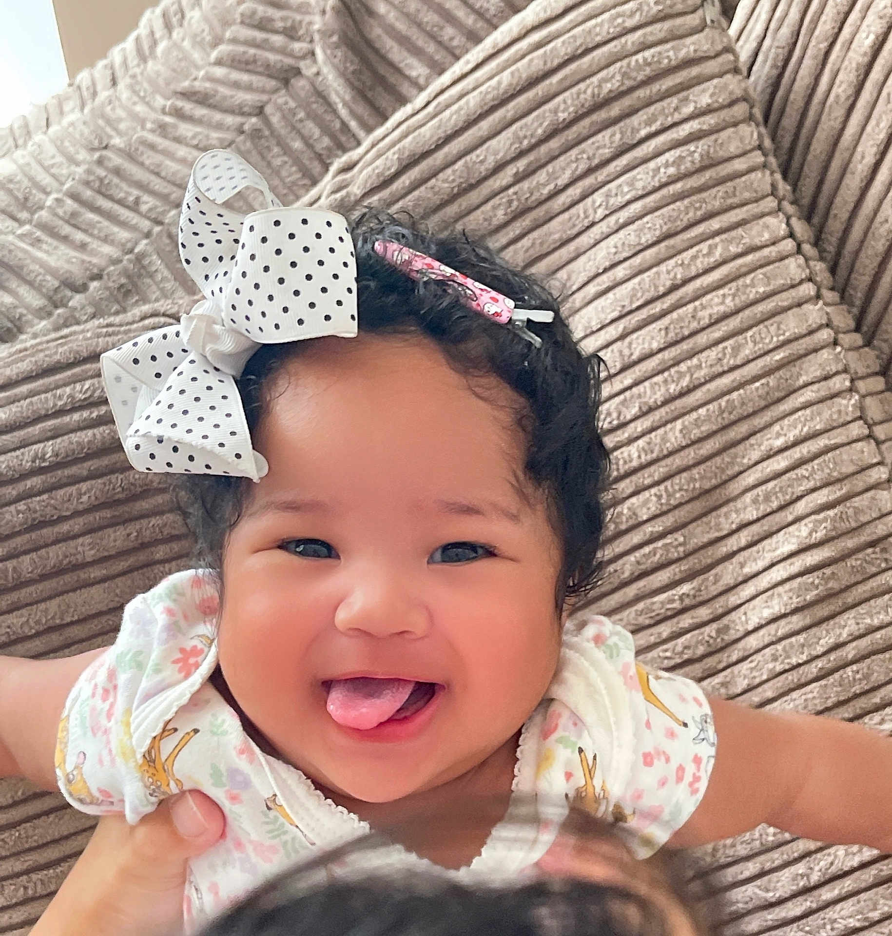 Magdalene is registered to the contest to win money with this photo: baby, child, smiling, tongue_out, bow, hair_accessory, curly_hair, infant, cute, happy, person, portrait, indoor, couch, clothing, hand, playful, face, skin, young