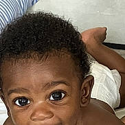 Kyzier Williams joined the competition — help win amazing prizes! baby, child, curly_hair, tongue_out, smiling, face, eyes, skin, bed, pillow, diaper, happy, cute, infant, lying_down, closeup, person, indoors, playful, young_child
