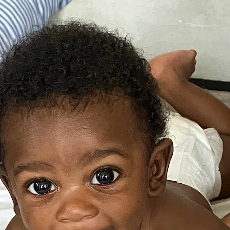 Kyzier Williams joined the competition — help win amazing prizes! baby, bed, child, closeup, curly_hair, cute, diaper, eyes, face, happy, indoors, infant, lying_down, person, pillow, playful, skin, smiling, tongue_out, young_child