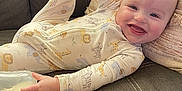 Weston is registered to the contest to win money with this photo: baby, infant, smiling, pajamas, animal_print, bottle, milk, couch, pillow, cozy, happy, child, relaxed, indoors, cute, playful, face, hand, foot, person