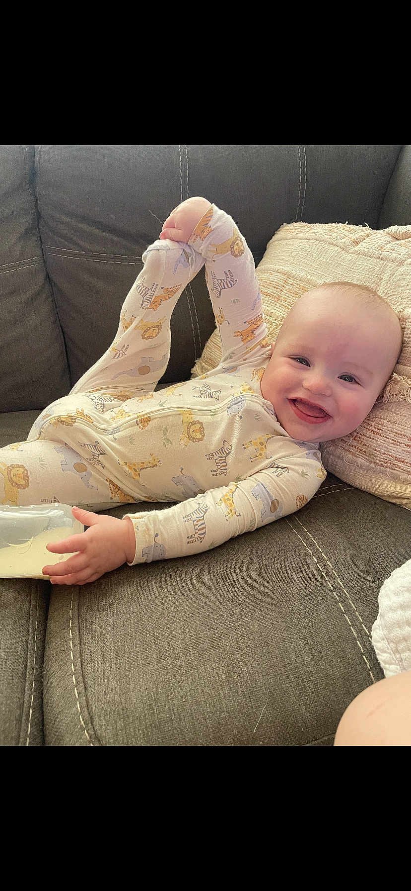 Weston is registered to the contest to win money with this photo: baby, infant, smiling, pajamas, animal_print, bottle, milk, couch, pillow, cozy, happy, child, relaxed, indoors, cute, playful, face, hand, foot, person
